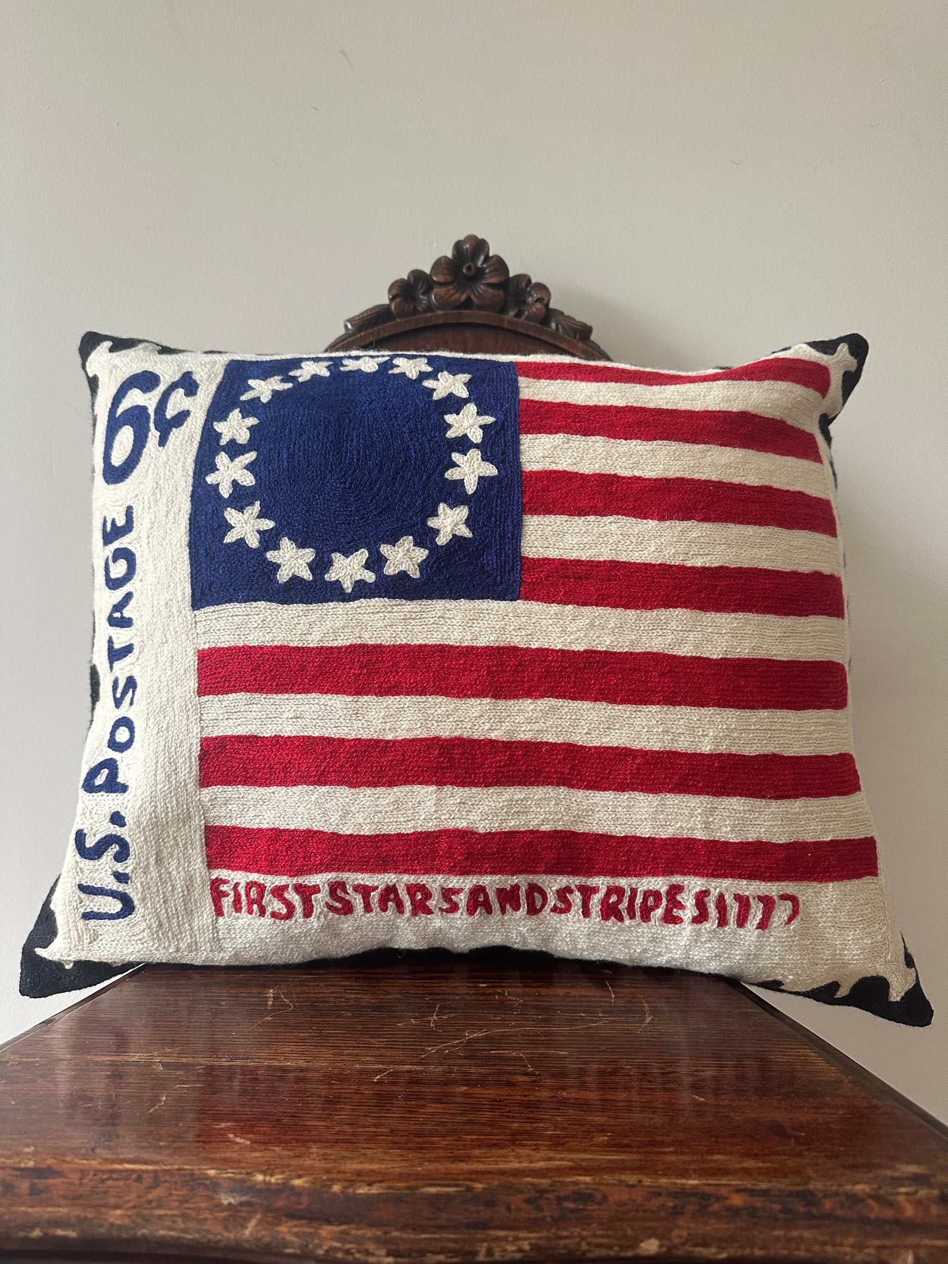 A rectangular decorative throw pillow featuring a vintage-style American flag design with 13 stars in a circle, red and off-white stripes, and text reading 'U.S.